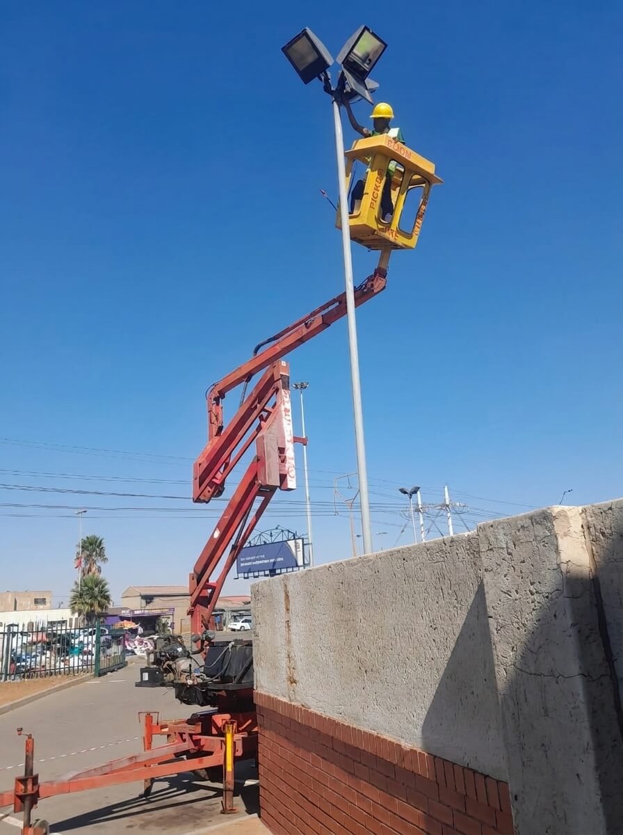 High-mast electrical works and lighting maintenance using a cherry picker with safety helmet PPE.